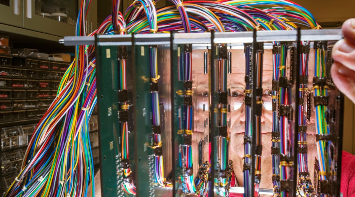 Materials scientist Paul Vianco peers through an experimental setup of printed wiring assemblies used to validate solder modeling in a Sandia National Laboratories project to study solder failure. Computational modeling of solder joint fatigue is also critical to Sandia&rsquo;s role in life extension programs for nuclear weapons.