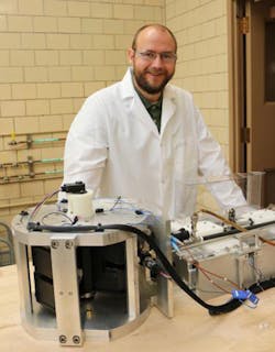 Lucas Griffith, a researcher at Ames National Lab, sits next to CaloriSMART, a device that tests a material&rsquo;s exergetic quotient&mdash;a measure of how strong a material&rsquo;s magnetocaloric effect is.