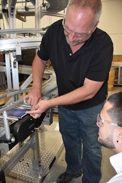 An engineer shows a trainee how the transfer point on a plastic chain conveyor works.