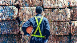 Worker standing in front of plastic waste bales Worker standing in front of plastic waste bales