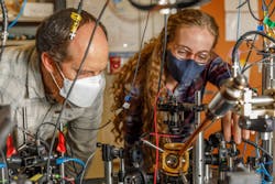 Peter Schwindt, a Sandia National Laboratories scientist (left), and postdoctoral scientist Bethany Little examine the vacuum package held in a yellow, 3D-printed mount. Peter Schwindt, a Sandia National Laboratories scientist (left), and postdoctoral scientist Bethany Little examine the vacuum package held in a yellow, 3D-printed mount.