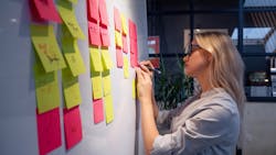 Person writing on a sticky note on a wall of notes Person writing on a sticky note on a wall of notes