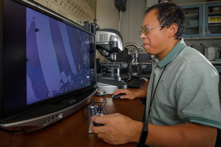 Sandia National Laboratories researcher Guangping Xu uses an optical microscope to examine unusually hard coatings made at the lab. The immediate goal is to develop better, less-expensive protection from fast-moving debris scattered by Sandia&rsquo;s Z machine when it fires.