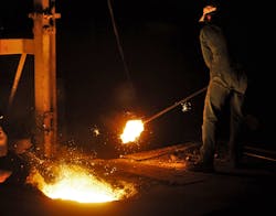 A worker in a factory making cast iron parts stands close to the melting pit.