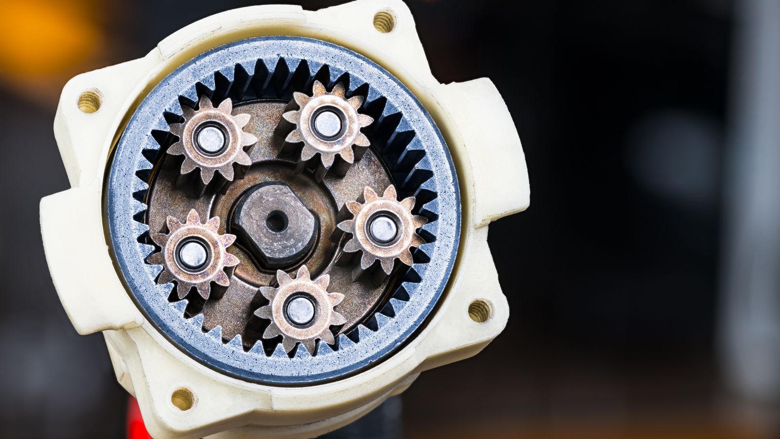Metal cog wheels in open planetary gearbox of power drill on dark background