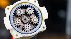 Metal cog wheels in open planetary gearbox of power drill on dark background