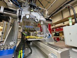 A closeup view of the Y axis, center, and the Z and X axes, above. On the Z axis from left to right are the Nordson adhesive applicator, Banner vision system and plasma gas applicator. The pick-and-place guided actuator is mounted behind the plasma applicator and is not easily distinguished. A box of die-cast housings is visible on the lower left. A closeup view of the Y axis, center, and the Z and X axes, above. On the Z axis from left to right are the Nordson adhesive applicator, Banner vision system and plasma gas applicator. The pick-and-place guided actuator is mounted behind the plasma applicator and is not easily distinguished. A box of die-cast housings is visible on the lower left.